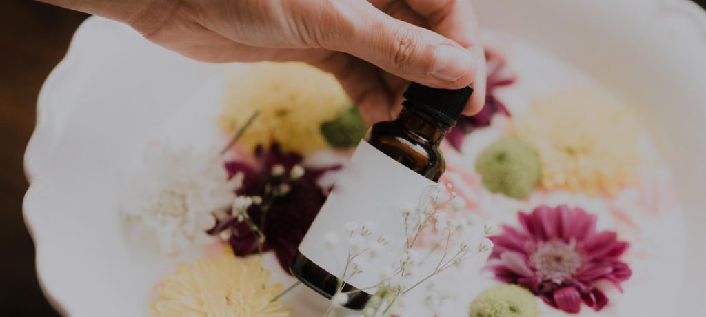 A person holding an essential oil bottle over a bowl of flowers.