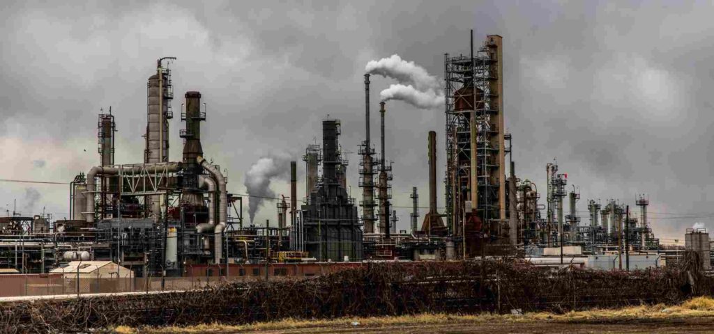 chemical plant with multiple smokestacks emitting smoke into a grey cloudy sky