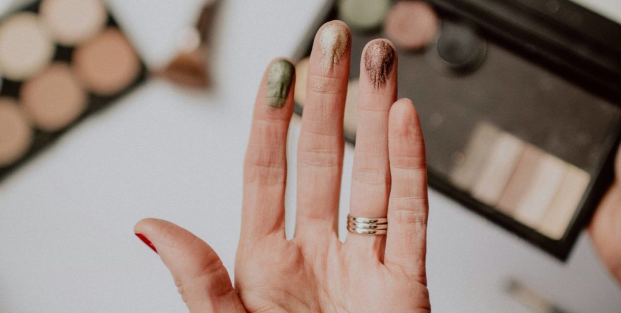 A close-up of a hand with fingers that have different shades of makeup or powder on them.