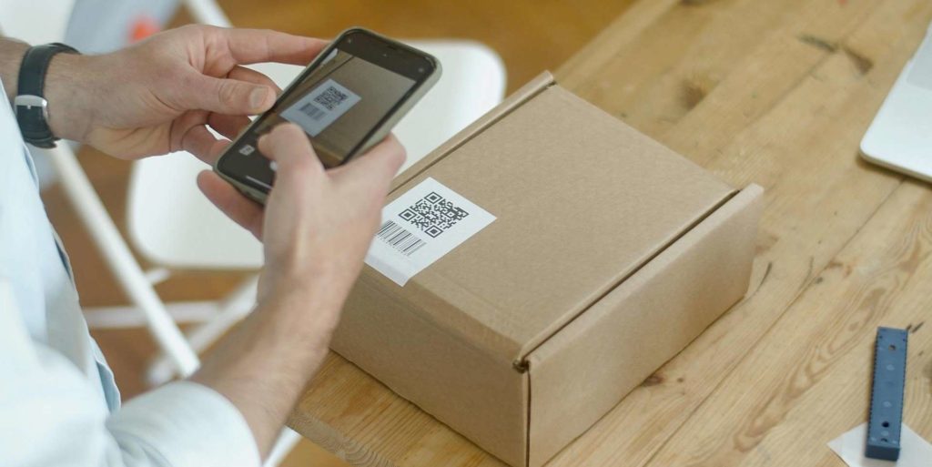 A person scanning a QR code on a cardboard package using a smartphone.