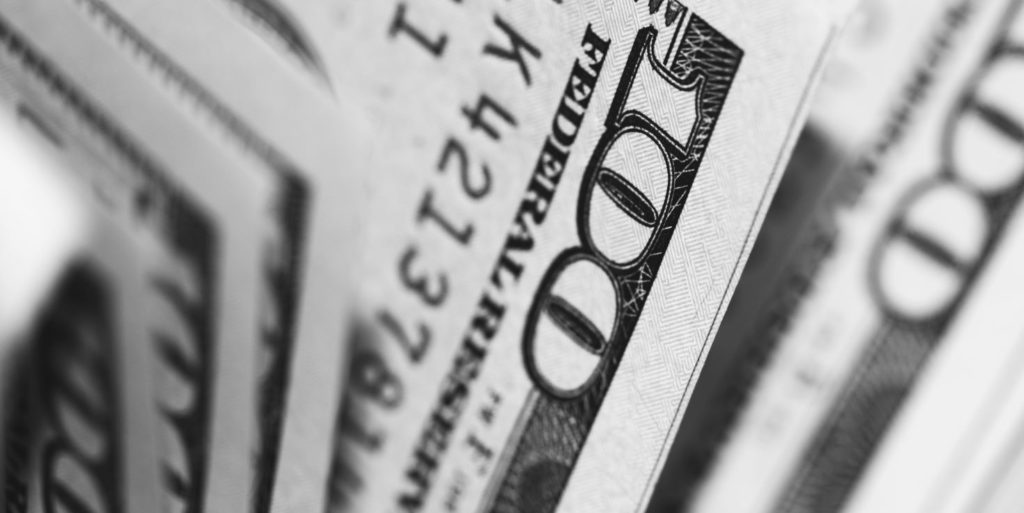 A close-up, black-and-white photo of stacked U.S. one-hundred dollar bills