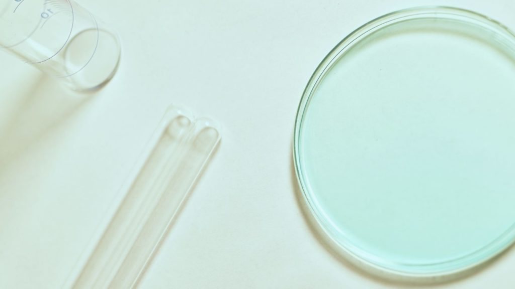 A top-down view of laboratory equipment, including a clear petri dish, glass test tubes, and a measuring cylinder