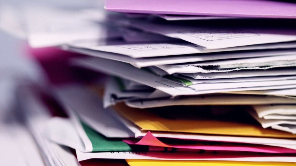 A large stack of papers, envelopes, and sticky notes in various colors.