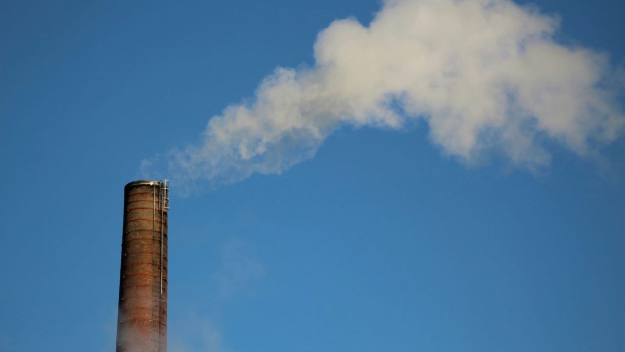 An industrial chimney releasing white smoke against a clear blue sky.