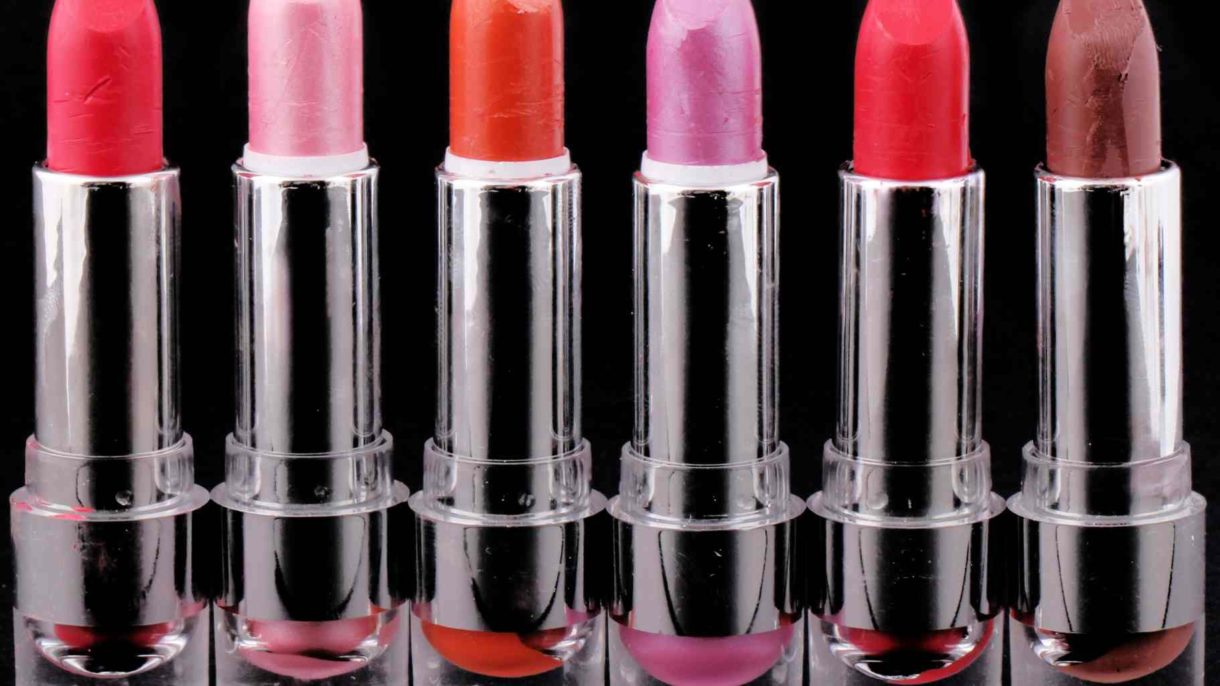 A row of six lipsticks in different colors, lined up on a black background.