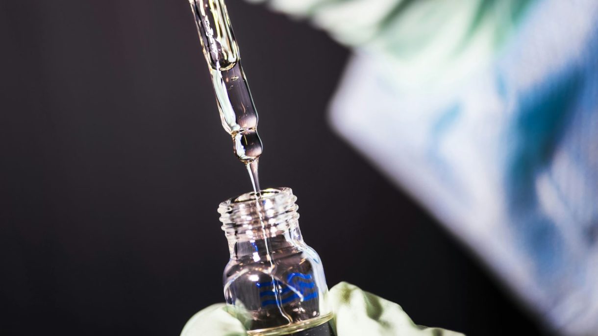 A gloved hand using a pipette to transfer a liquid into a small vial - challenge test in cosmetics