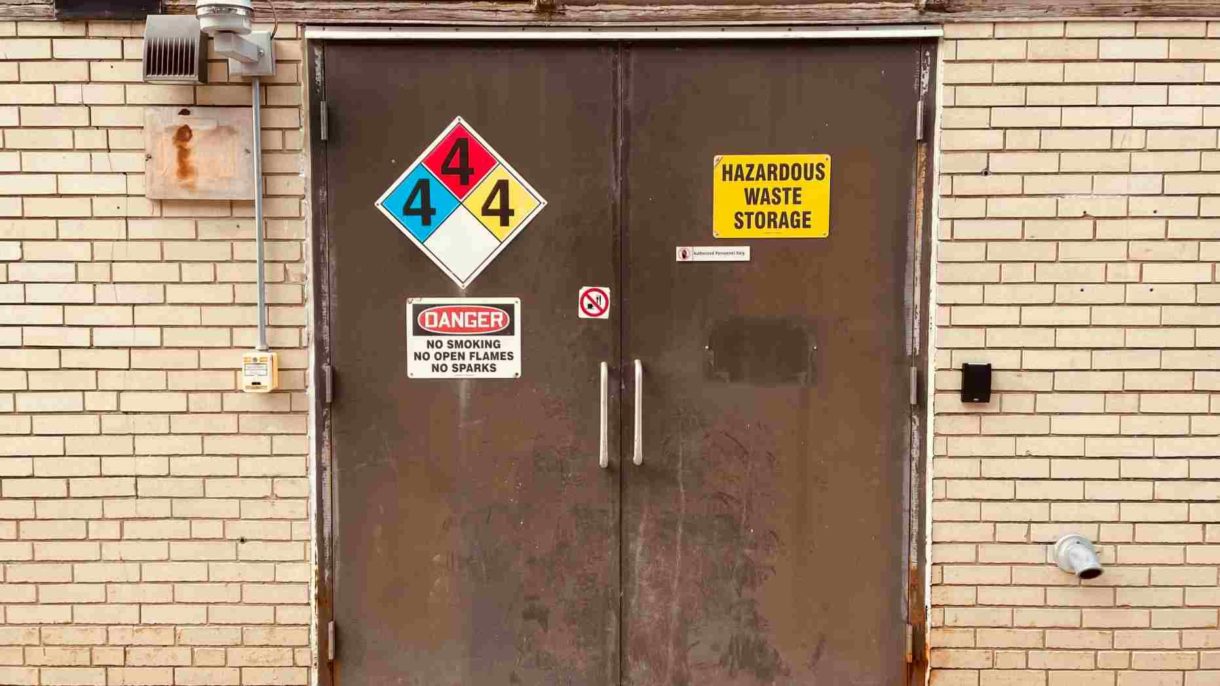 A pair of metal double doors with several signs and markings on them like "Hazardous Waste Storage" -Chemicals CLP