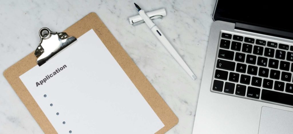 image of an application form next to a laptop on a white table