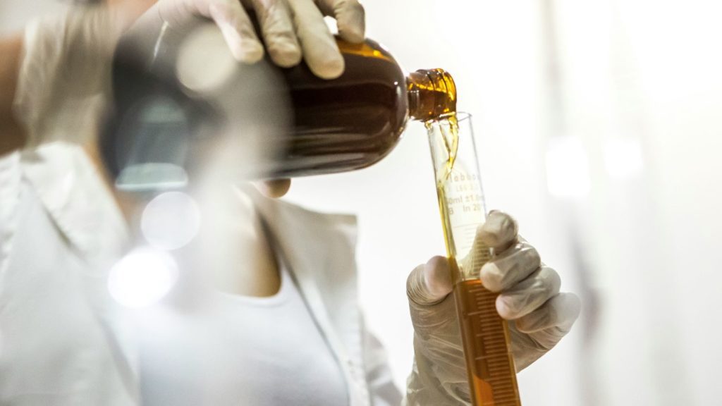a scientist pouring a brown liquid in a test tube