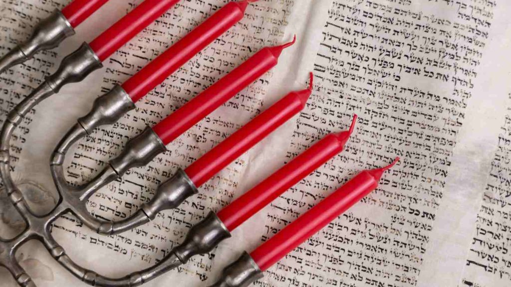 A menorah with red candles rests on an open Hebrew scripture