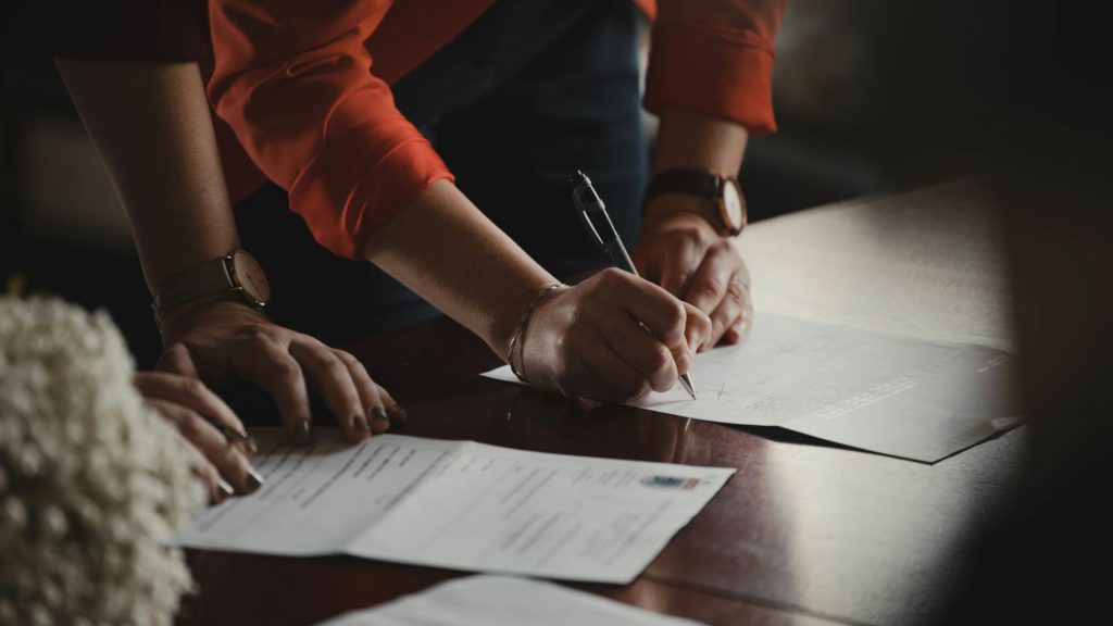 A person in a red shirt signing documents