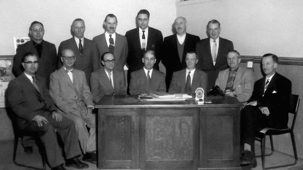 A black and white archive image of men in suits sitting behind a desk