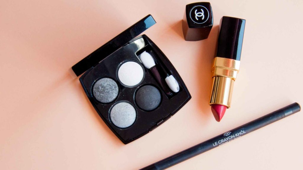 A make box, a lipstick and an eyeliner on a flat pink surface