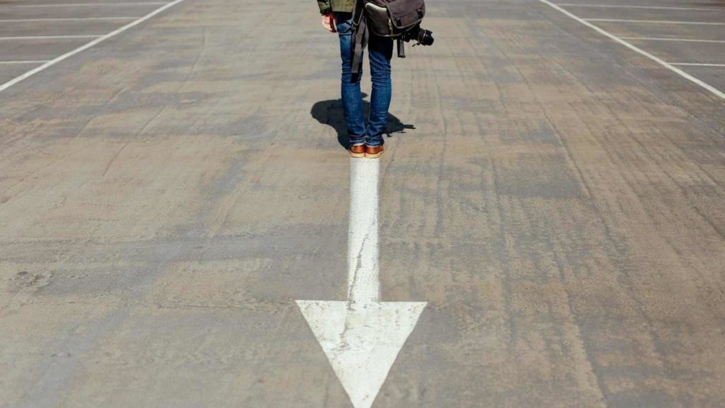 A man standing at the tail end of a white arrow painted on pavement