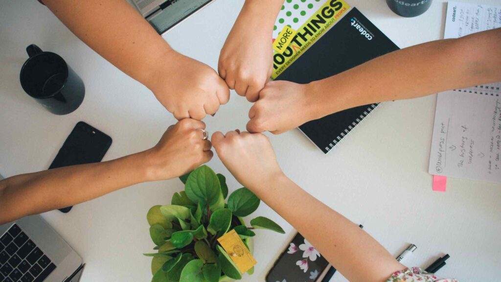 five people bringing their fists together above a desk