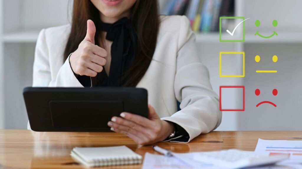 A business woman sitting at a desk, holding a tablet and giving the thumbs up