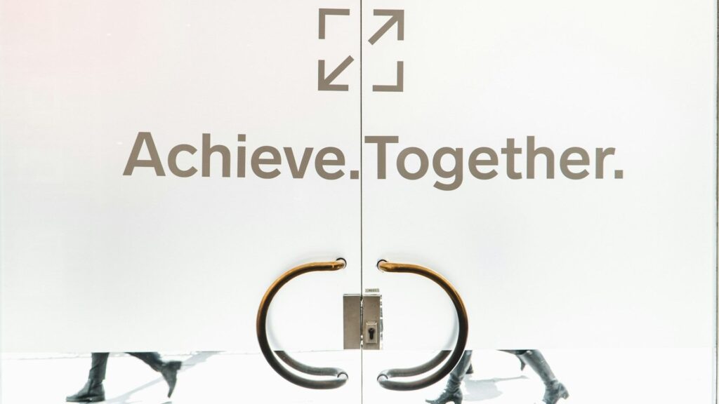 Close-up of a glass door with the message achieve together written on it